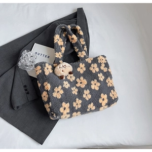 Detailed macro view of dark grey plush tote bag with yellow floral patterns and plush charm