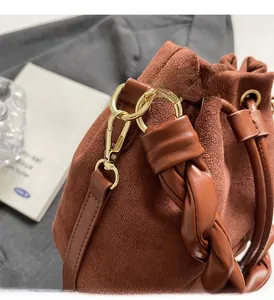Detail of brown suede bucket bag featuring woven handle and gold metal hook hardware