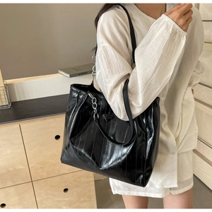 Detail of black patent leather tote bag with silver chain strap and metal triangle emblem