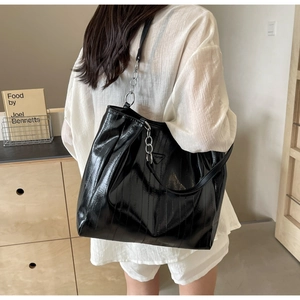 Detailed view of black patent leather tote bag with vertical stripes and silver chain