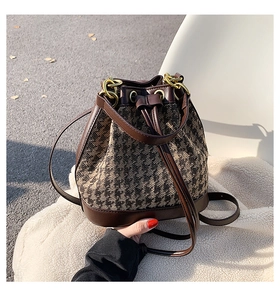 Detailed view of a woven bucket bag featuring brown leather trim and gold metal hardware