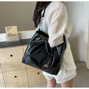 Side view of large black glossy leather tote bag with thick silver chain on woman shoulder