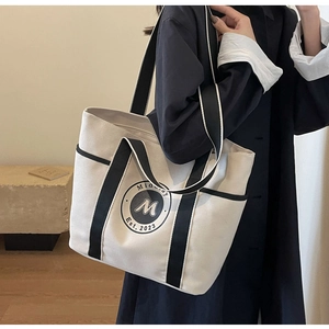 Detalle del bolso tote de lona blanco roto con asas negras y logotipo circular impreso
