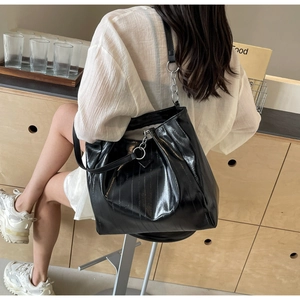 Detail of a large black tote bag featuring glossy crinkled leather and silver chain strap