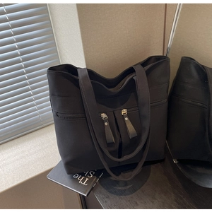 Dettaglio borsa tote in tela nera con due tasche frontali simmetriche dotate di cerniera