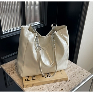 Detail of cream tote bag with crocodile texture, silver chain strap and logo plaque