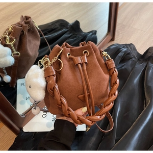 Detail of a brown suede bucket bag with woven handle and fluffy cloud charm accessory