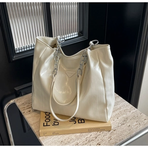 Close-up of beige glossy tote bag with vertical texture and silver chain strap details