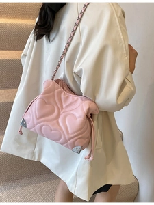 Pink heart quilted shoulder bag with silver chain strap worn by a model in a side view