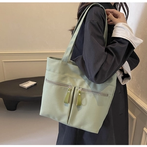 Dettaglio della borsa tote in tela verde chiaro con due tasche frontali e tiretti oliva