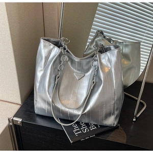 Close-up of silver tote bag with pleated texture and triangular metal plaque detail
