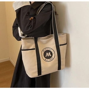 Vista lateral del bolso tote de lona con ribete negro en el hombro de la modelo