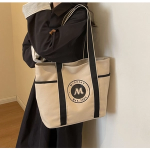 Detalle del bolso tote grande de lona con logotipo vintage y asas de cincha de color negro