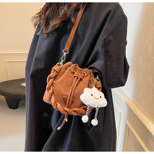 Detail of a brown suede bucket bag with woven handle and a white cloud plush charm