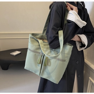 Dettaglio della borsa tote in tela verde chiaro con doppie tasche frontali e tiretti in pelle