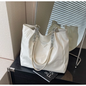 Detail of a creamy white textured tote bag featuring chain handles and metal logo plaque