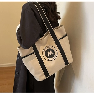 Detalle del bolso tote de lona con bolsillos laterales y logo al hombro