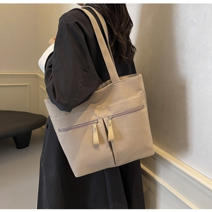 Dettaglio borsa tote in tela beige con tasche a zip multipli indossata sulla spalla