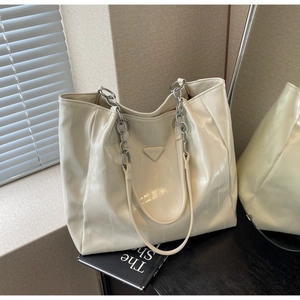 Detail of off-white patent leather tote bag with crinkle texture and metal chain strap