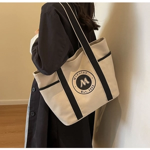 Detalle del bolso tote de lona crema con correas negras y logotipo en el hombro