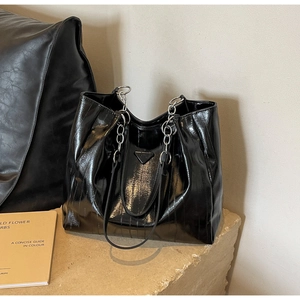 Detail of high-gloss black patent leather tote with silver chain and metal triangle