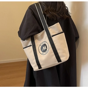 Detalle de bolso tote de lona con bolsillo lateral y logo visto de perfil en persona