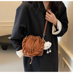 Detail of brown suede bucket bag featuring woven handle and cute cloud plush charm