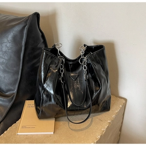 Detail of black textured tote bag with metal triangle plaque and chain strap