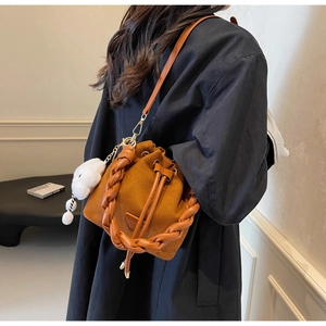 Detail of a brown suede bucket bag with a braided handle and a white fuzzy pompom charm