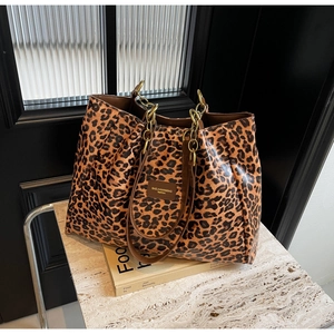 Close-up of leopard print tote bag featuring gold chain handle and brand logo patch