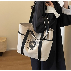 Vista lateral detallada de la bolsa tote de lona beige con ribete negro y logo Midolay