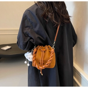 Close-up of caramel suede bucket bag with woven handle and plush cloud charm