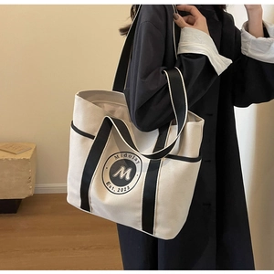 Primer plano de un bolso tote de lona crema con asas negras y un logotipo circular impreso