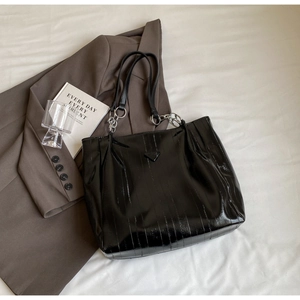 Close-up of black glossy tote bag with vertical stitching and silver chain detail