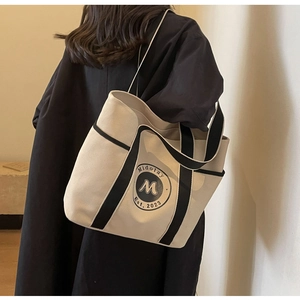 Detalle de un bolso tote de lona beige grande con ribetes negros usado por la modelo