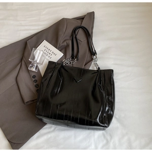 Close-up of black glossy tote bag with crinkle patent leather and chain straps