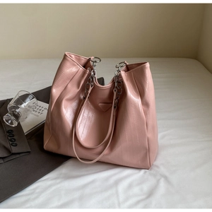 Close-up of pink tote bag with textured faux leather and chain strap on white bedding