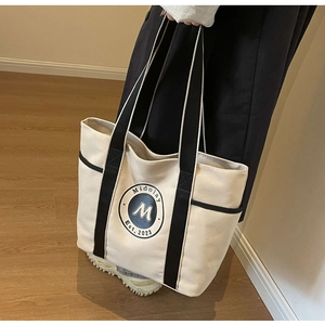 Primer plano del bolso tote de lona con correa negra y logotipo circular de Midolay