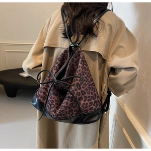 Leopard print backpack with leather drawstring and bow detail worn by a model in a trench coat
