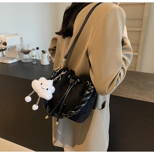 Detail of black drawstring bucket bag with plush charm and woven handle in café setting