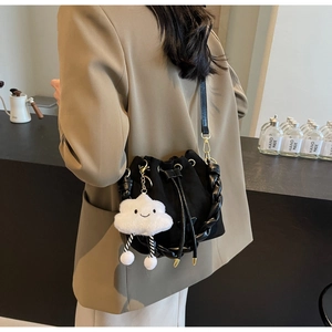 Detail of black suede bucket bag with drawstring closure and white cloud plush charm