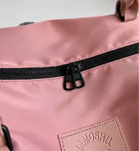 Détail du sac de voyage rose avec doubles fermetures éclair noires et logo embossé élégant