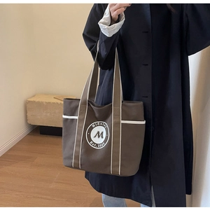 Detalle del bolso tote de lona marrón oscuro con ribetes blancos y logotipo circular frontal
