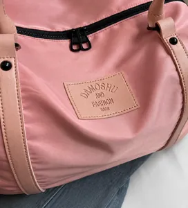 Gros plan du sac de voyage rose avec étiquette en cuir gaufrée et double fermeture