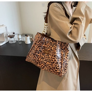 Leopard print tote bag with gold chain strap shown on a model in a cozy cafe setting