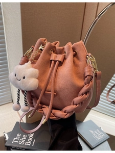 Pink suede bucket bag with woven handle and plush cloud charm on a lifestyle background