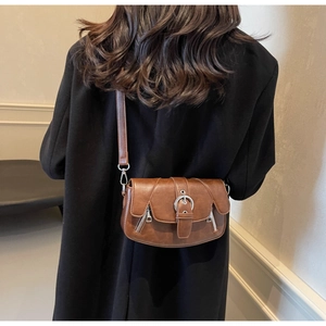 Detail view of vintage brown saddle bag with silver buckle and metallic zipper accents