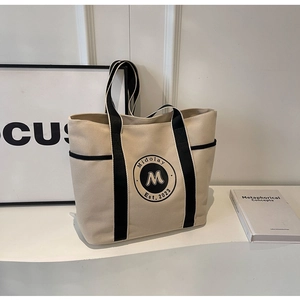 Primer plano de un bolso tote de lona beige con ribete negro y detalle del logo Midolay