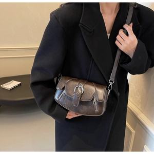Detail of dark brown saddle bag with silver ring buckle on model wearing black coat