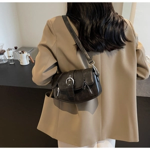 Close-up of retro brown saddle bag with silver metal buckle on model in beige blazer